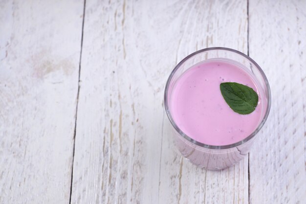 Glasschale mit Blaubeerjoghurt und Minze auf einem hellen Holztisch. Gesundes Frühstück an einem schönen Morgen