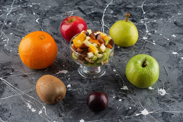 Glasschale mit geschnittenem gemischten Salat mit ganzen frischen Früchten auf einem Marmortisch.