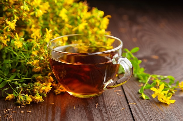 Glasschale mit Hypericum perforatum, Johanniskraut oder Tutsan-Pflanzengetränk mit frischen Blumen auf dunklem Holz