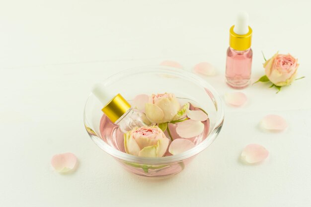 Glasschale mit Rosenwasser, Blumen und Rosenblättern, Kosmetikflaschen mit Zfir-Blumenöl. Aromatherapie, Anti-Stress.