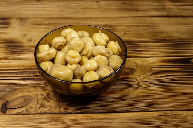 Glasschüssel mit eingelegten Champignons. Marinierte Pilze auf Holztisch