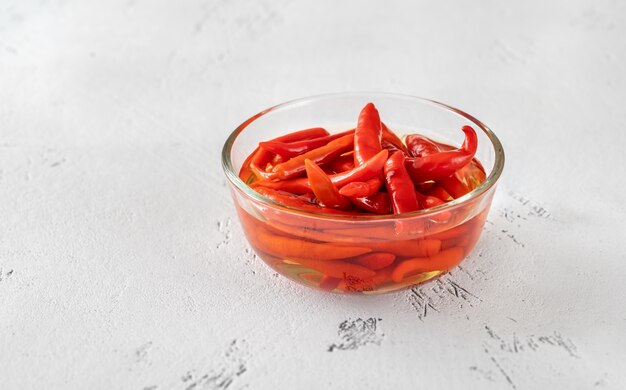 Glasschüssel mit eingelegten Chilischoten auf weißem Tisch