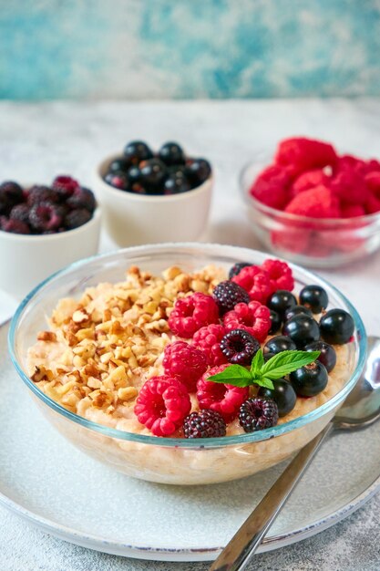 Foto glasschüssel mit haferflocken, verschiedenen beeren und zerkleinerten nüssen in einer glasschüssel, gesunde, ausgewogene ernährung