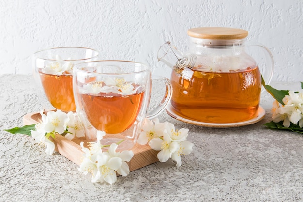 Glastasse mit doppeltem Boden der Vorderansicht mit duftenden Jasmintee-Jasminblüten und Teekanne aus Glas mit frisch gebrühter Tee-Teezeremonie