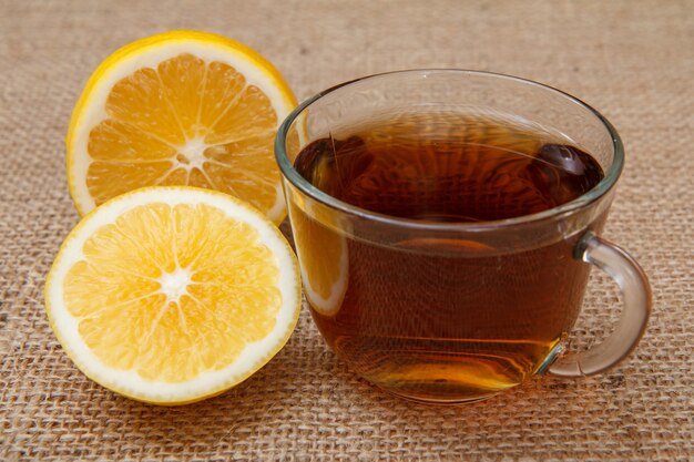 Glastasse Tee und Zitronenstücke auf dem Tisch mit Sackleinen.