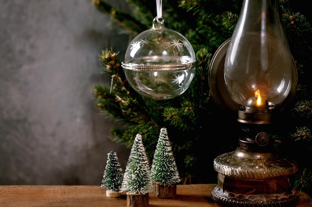 Glastransparente leere Öffnungskugel für Geschenk- oder Produktanzeige, dekorative Weihnachtsbäume Vintage Kerosinlampe auf Holztisch, Tannenbaum im Hintergrund. Werbekonzept für Neujahrsfeiertage