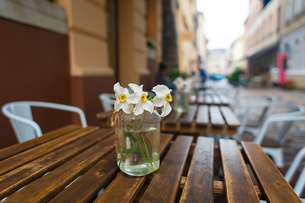 Glasvase mit Blumen auf dem Holztisch des Restaurants auf der Straße. Dekordetails, die Gemütlichkeit schaffen