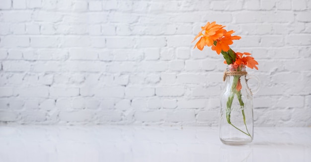 Glasvase mit orange schöner Blume auf weißem Tisch.