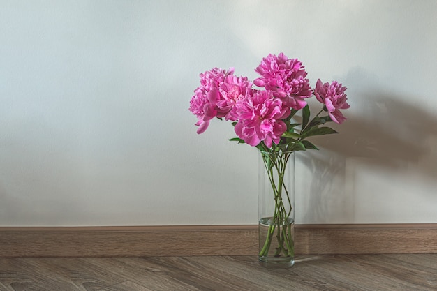 Foto glasvase mit rosa pfingstrosen auf holzboden