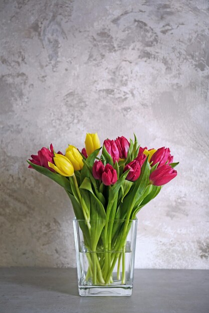 Glasvase mit Strauß schöner Tulpen auf farbigem Hintergrund