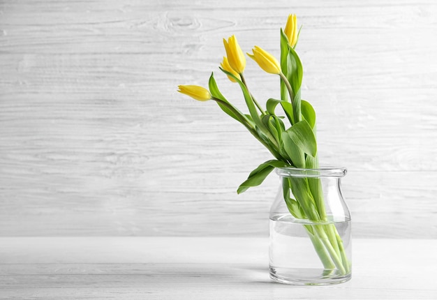 Glasvase mit Strauß schöner Tulpen auf farbigem Hintergrund