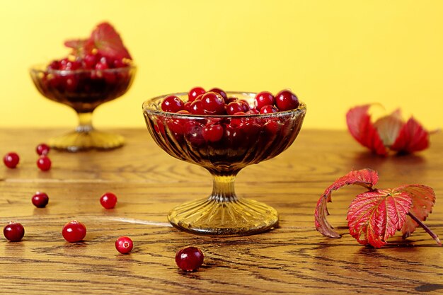 Glasvasen mit reifen Preiselbeeren auf einem Holztisch gelber Hintergrund