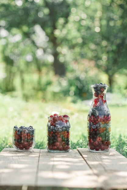 Glaswaren mit frischen Beeren auf einer alten Holzbank Frische Gartenbeeren Heidelbeere-Johannisbeer-Kirsche