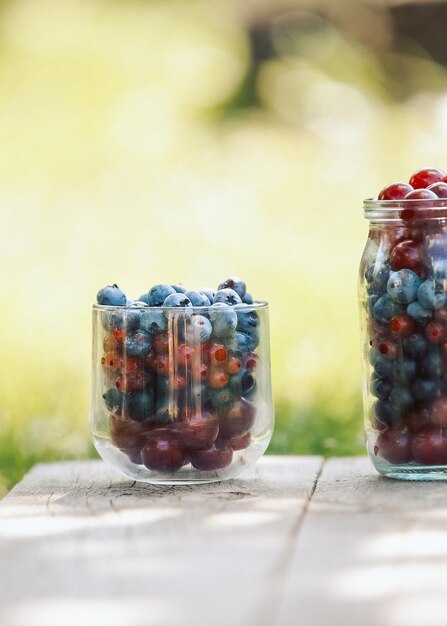 Glaswaren mit frischen Beeren auf einer alten Holzbank Frische Gartenbeeren Heidelbeere-Johannisbeer-Kirsche