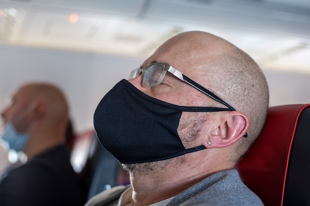 Glatzköpfiger Mann in schwarzer medizinischer Maske und Brille schläft im Flugzeug schlafender Tourist im Flugzeug