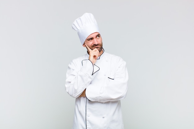 Glatzköpfiger Mann mit einem konzentrierten Blick, der sich mit einem zweifelhaften Ausdruck wundert und nach oben und zur Seite schaut