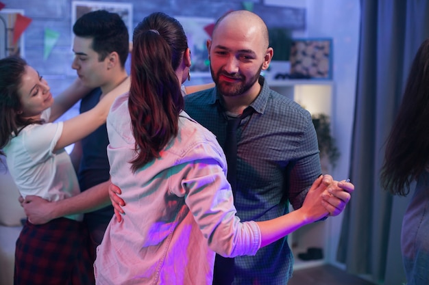 Glatzköpfiger Mann tanzt mit seiner Frau auf der Party von Freunden.