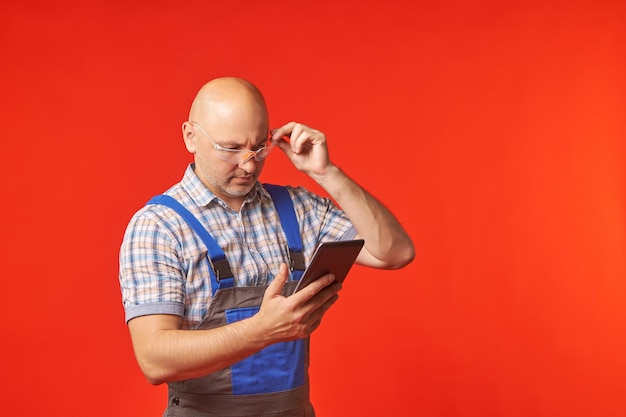 Glatzkopf in Arbeitskleidung hält ein Telefon in der Hand und arbeitet mit dem anderen darin