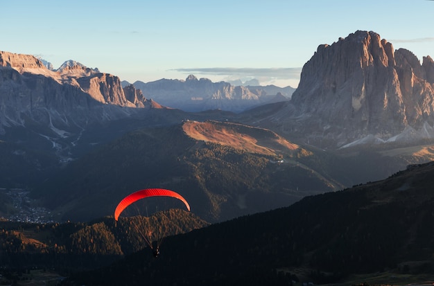 Gleitschirm mit rotem Fallschirm fliegt über die Berge, die mit Bäumen im Sonnenlicht gefüllt sind.