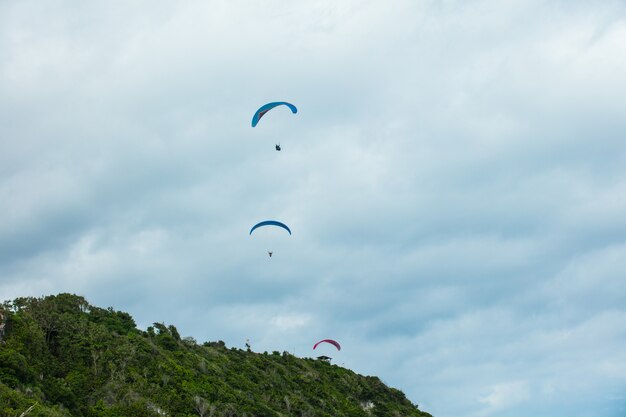 Gleitschirmflieger, die von einem grünen Berg vor blauem Himmel mit Wolken abheben