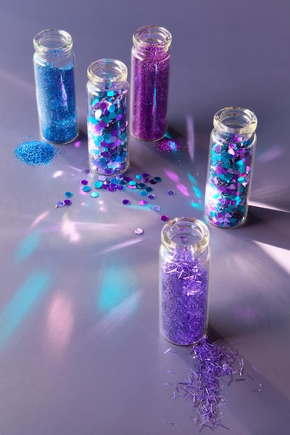 Glitzerprodukte in transparenten Flaschen Nahaufnahme Verschiedene Glitzerpulver und Partikel in neonblauen, violetten und türkisfarbenen Farbtönen auf dunklem Hintergrund
