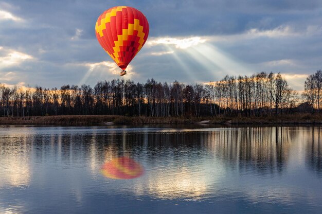 Globo de aire caliente brillante vuela sobre el lago en otoño