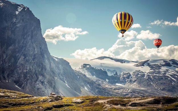 un globo de aire caliente volando sobre una montaña con una casa en el fondo