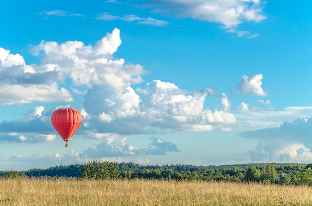 Un globo de avión rojo vuela muy lejos en el horizonte de un cielo azul con nubes