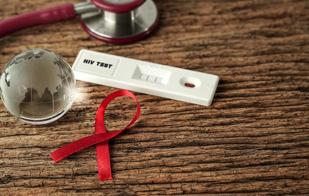 Foto globo de cristal de cinta roja kit de prueba de vih borrosa sobre fondo de madera concepto del día mundial del sida