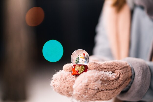 Globo de neve de vidro de ano novo nas mãos. tempo feliz na floresta. luzes festivas de guirlanda