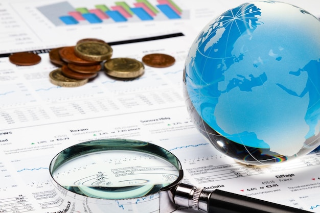 Foto globo, lupa y monedas en los informes financieros en primer plano