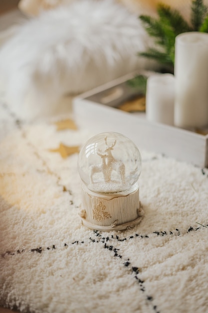 Globo de nieve de cristal mágico con ciervos y una guirnalda sobre una alfombra mullida en un interior luminoso.
