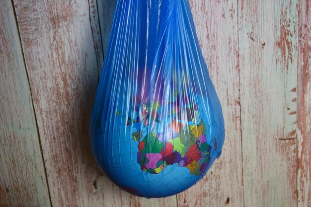 El globo del planeta Tierra cuelga en una bolsa de basura de plástico azul sobre un fondo de tablones de madera