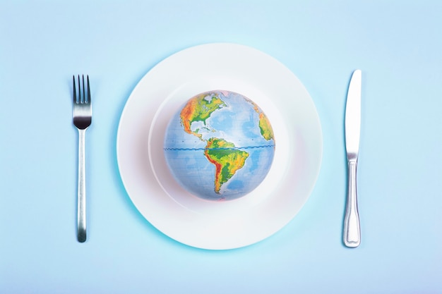 Globo en un plato para comida sobre un fondo azul. Poder, economía, política, globalismo, hambre, pobreza y concepto de alimentación mundial.