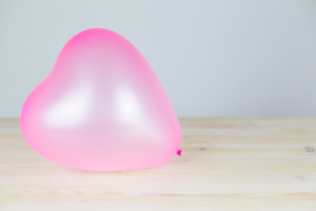 Globo rosa en forma de corazón descansa sobre una mesa de madera