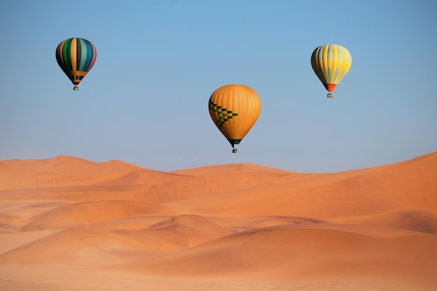 Globos de aire caliente de colores volando sobre las dunas de arena al atardecer