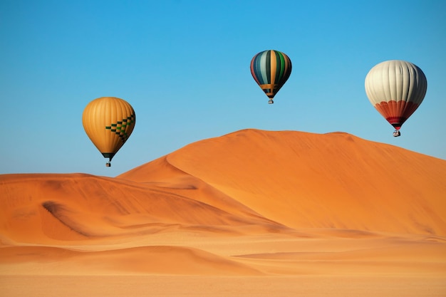 Globos de aire caliente de colores volando sobre las dunas de arena al atardecer