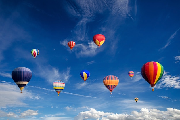 Globos coloridos del aire caliente que vuelan sobre las nubes blancas y el cielo azul.