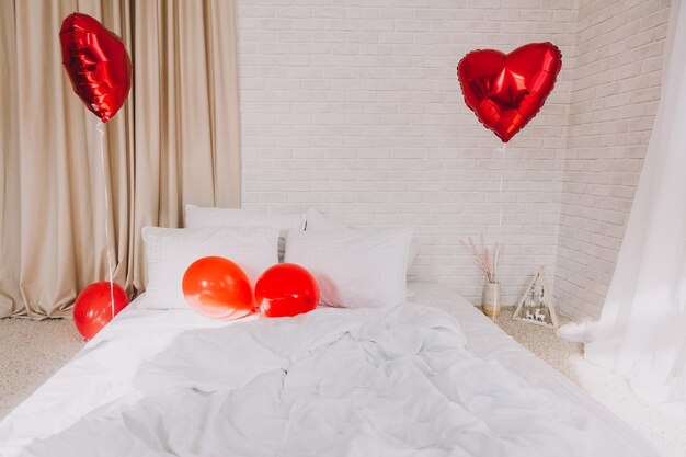 Globos de corazón rojo en un dormitorio con una cama blanca. día de San Valentín