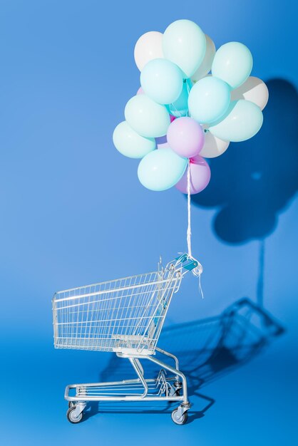 Globos decorativos atados a un carrito de compras vacío en azul.