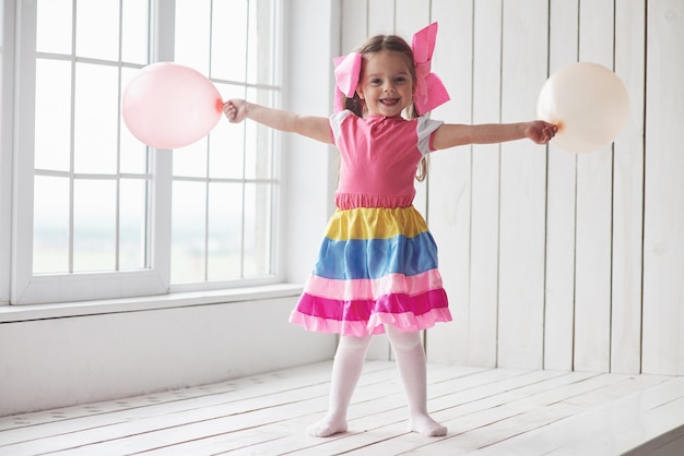 Globos fuera. Niño de pie junto a las ventanas en la habitación blanca y posando para la foto.