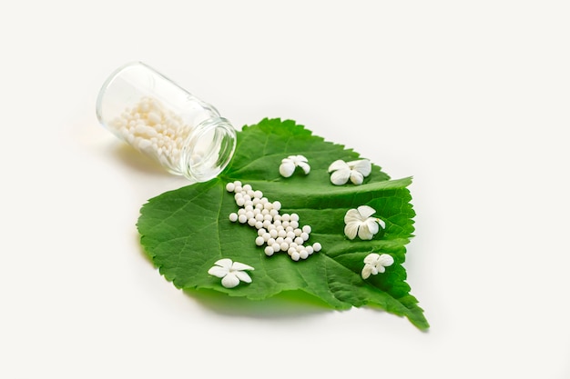 Glóbulos homeopáticos e frasco de vidro em uma folha de planta verde