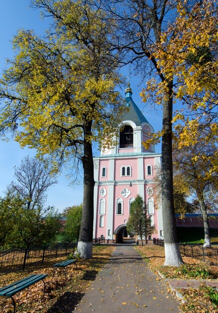 Glockenturm des Klosters Sviato-Troitskyi auf einem Hintergrund von Herbstbäumen in Gustynya. Gebiet Tschernihiw. Ukraine. Vertikal im Freien erschossen.