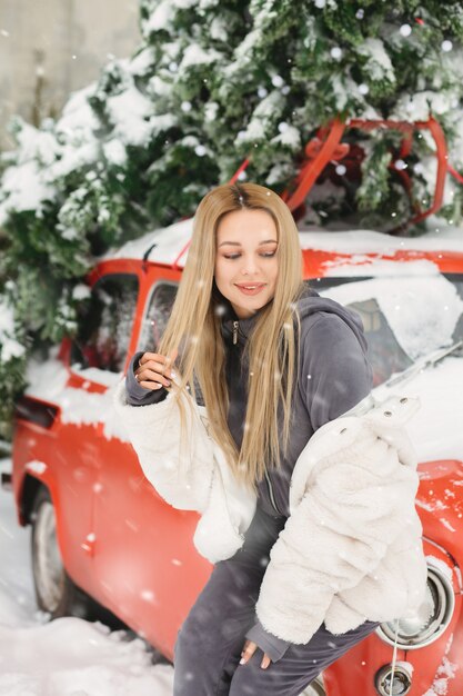 Gloriosa joven posando cerca de un coche rojo retro en tiempo de nieve