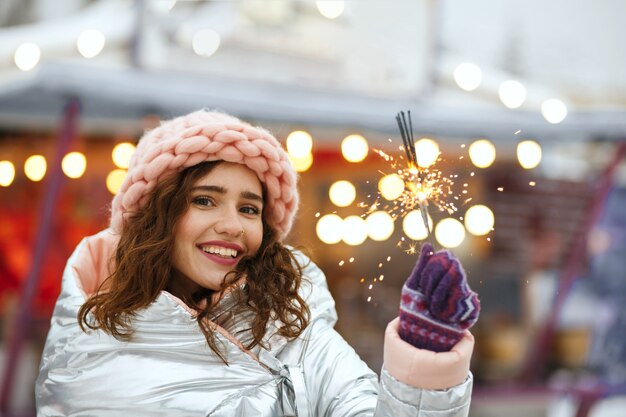 Foto gloriosa mujer morena con gorra rosa con luces de bengala. tiro al aire libre de invierno. espacio vacio