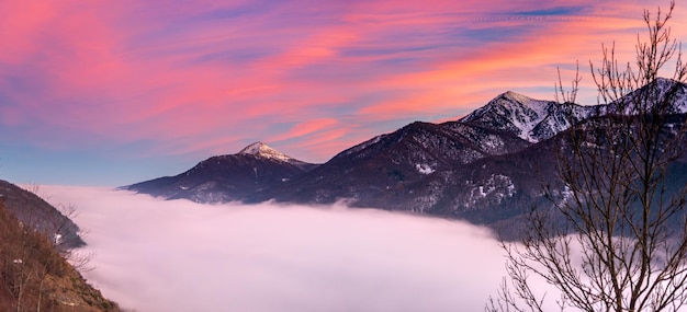 Glorious Sonnenuntergang in den italienischen Alpen Schöner Himmel über nebligen Tal und schneebedeckten Berggipfeln Winter in Piemont Italien
