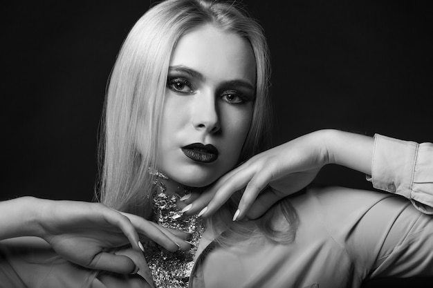 Glorreiches blondes Model posiert im Studio mit hellem Make-up und Folie am Hals. Monochrome Aufnahme