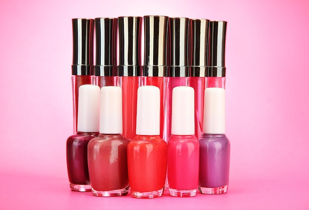 Gloss labiais lindos e frascos de esmalte em fundo rosa