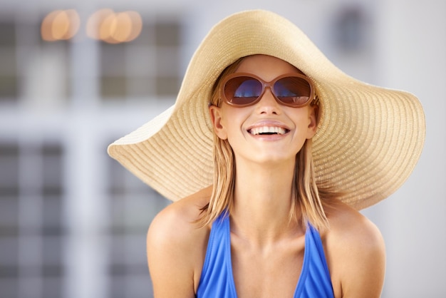 Glück am Pool Eine blonde Frau, die einen Sonnenhut trägt und in die Kamera lächelt