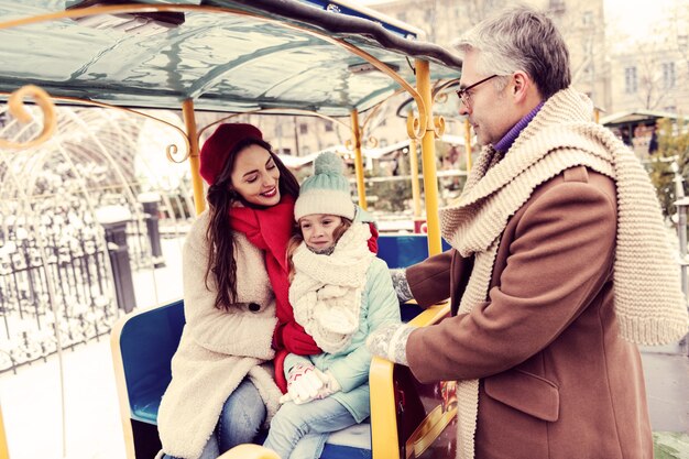 Glück ausdrücken. Erfreute brünette Frau, die Lächeln auf ihrem Gesicht hält, während sie ihr Kind ansieht